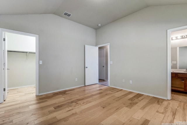 unfurnished bedroom with visible vents, connected bathroom, a walk in closet, vaulted ceiling, and light wood-style floors