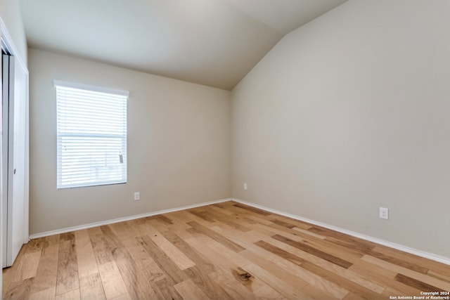 empty room featuring vaulted ceiling, baseboards, and light wood-style floors