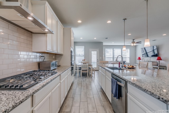 kitchen featuring appliances with stainless steel finishes, white cabinets, wall chimney exhaust hood, pendant lighting, and sink