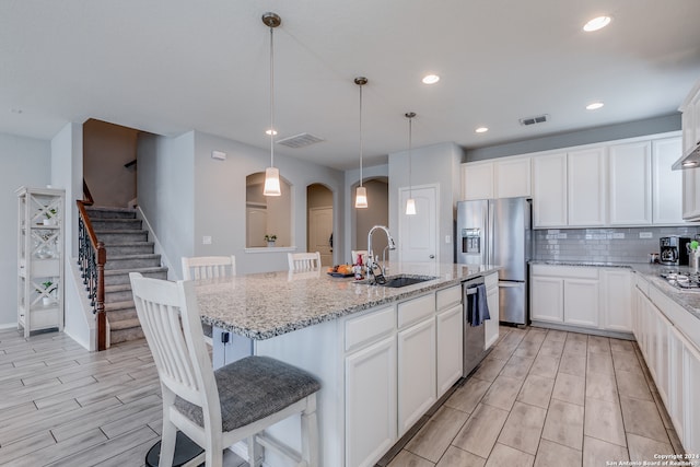 kitchen featuring hanging light fixtures, sink, a kitchen island with sink, appliances with stainless steel finishes, and light stone countertops