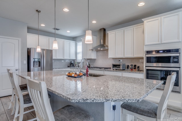 kitchen featuring wall chimney exhaust hood, white cabinets, appliances with stainless steel finishes, and a large island with sink