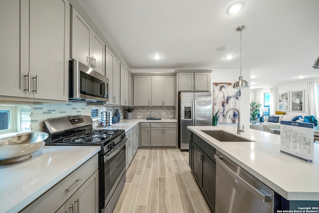 kitchen featuring appliances with stainless steel finishes, tasteful backsplash, gray cabinetry, sink, and decorative light fixtures