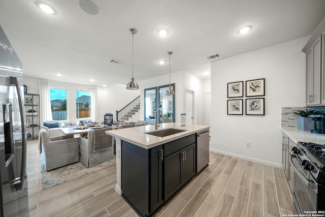 kitchen featuring sink, stainless steel appliances, light hardwood / wood-style flooring, an island with sink, and pendant lighting