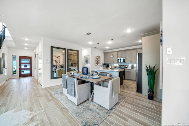 kitchen featuring stainless steel appliances, hanging light fixtures, an island with sink, gray cabinets, and light wood-type flooring