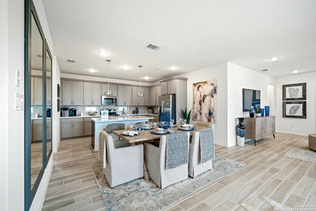 kitchen featuring tasteful backsplash, stainless steel appliances, decorative light fixtures, light hardwood / wood-style flooring, and an island with sink