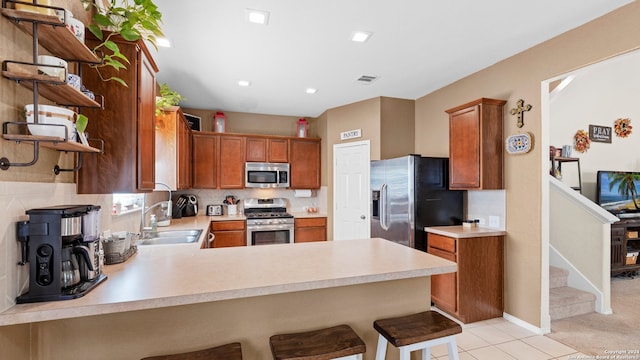 kitchen with sink, kitchen peninsula, a breakfast bar, light tile patterned flooring, and appliances with stainless steel finishes