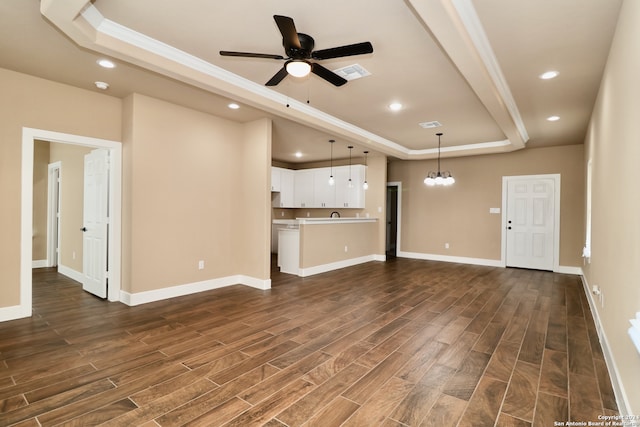 unfurnished living room featuring ceiling fan with notable chandelier, a tray ceiling, and dark wood-type flooring