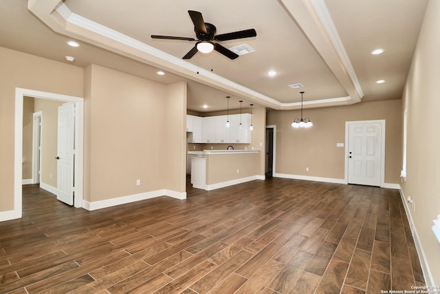unfurnished living room featuring a tray ceiling, recessed lighting, dark wood-style flooring, and ceiling fan with notable chandelier