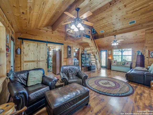 living room featuring lofted ceiling with beams, wooden walls, hardwood / wood-style flooring, and a barn door