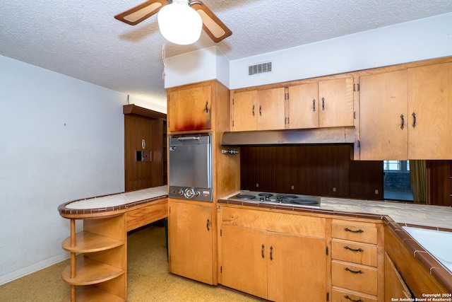 kitchen with a textured ceiling, stainless steel cooktop, ceiling fan, and tile countertops