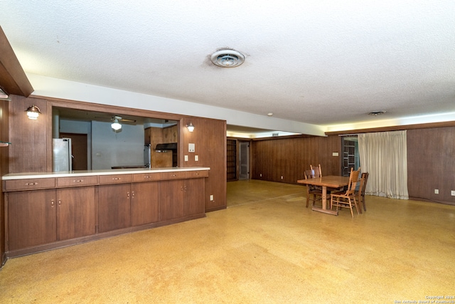 kitchen featuring wood walls, a textured ceiling, ceiling fan, and stainless steel refrigerator