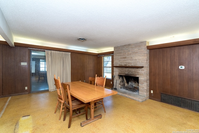 dining room featuring a textured ceiling, a stone fireplace, and wooden walls