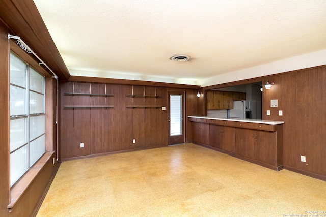 kitchen with wood walls, a textured ceiling, and white refrigerator with ice dispenser