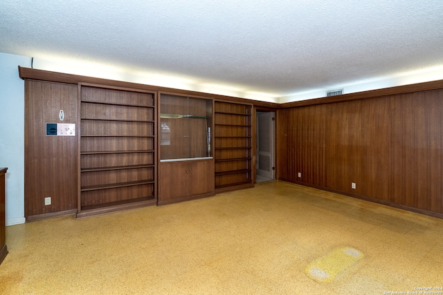 unfurnished living room featuring a textured ceiling and wood walls