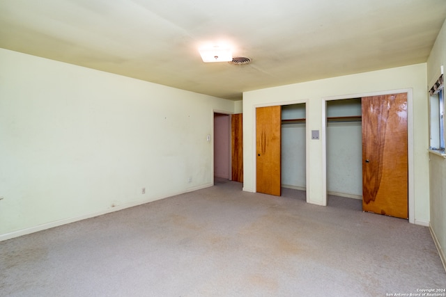 unfurnished bedroom with light colored carpet and two closets