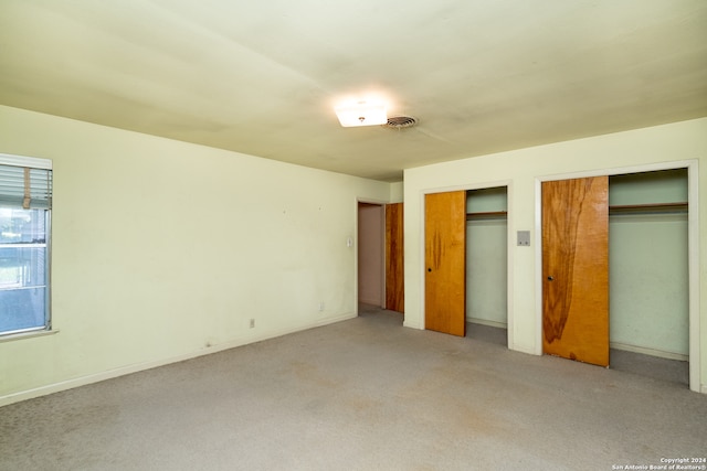 unfurnished bedroom featuring light carpet and two closets