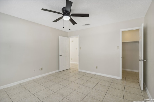 unfurnished bedroom with a closet, ceiling fan, a walk in closet, and a textured ceiling