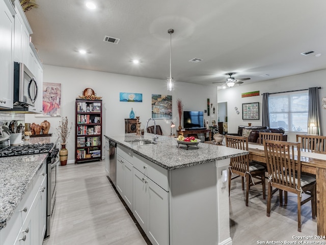 kitchen with light stone counters, white cabinets, stainless steel appliances, a center island with sink, and sink