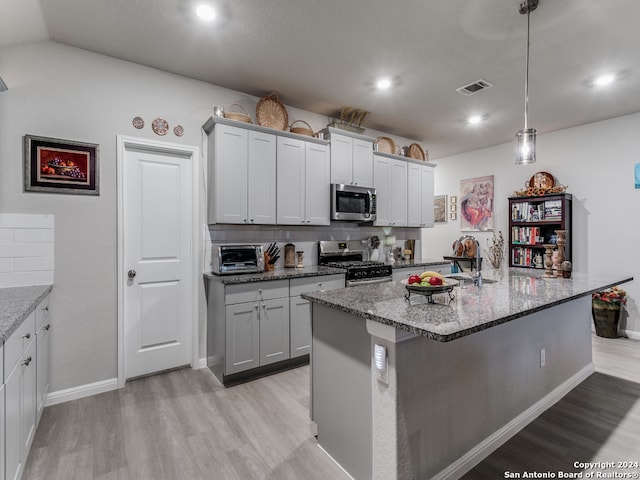 kitchen with an island with sink, appliances with stainless steel finishes, and hanging light fixtures