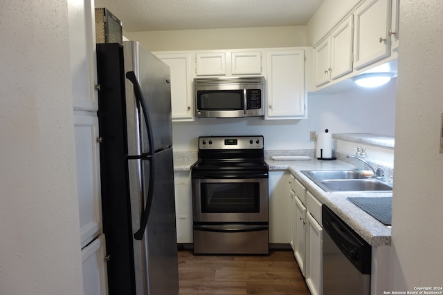 kitchen with appliances with stainless steel finishes, white cabinets, dark hardwood / wood-style flooring, a textured ceiling, and sink