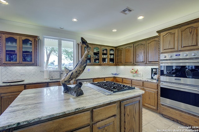 kitchen featuring light tile patterned flooring, light stone counters, backsplash, stainless steel appliances, and crown molding