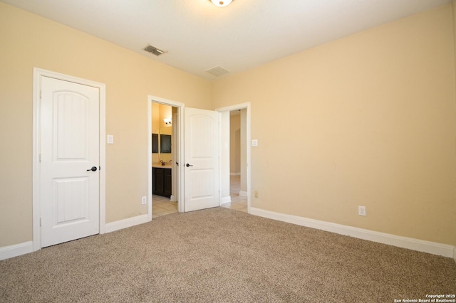 unfurnished bedroom featuring light colored carpet and connected bathroom