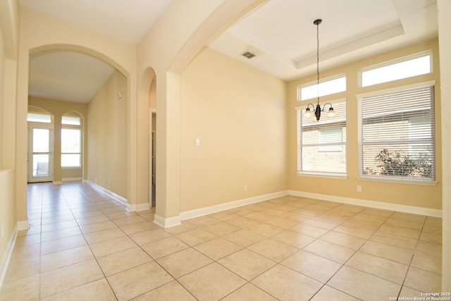 spare room with a tray ceiling, a healthy amount of sunlight, light tile patterned floors, and a chandelier