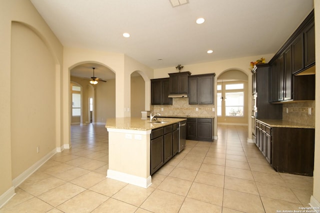 kitchen featuring light tile patterned flooring, tasteful backsplash, ceiling fan, and an island with sink