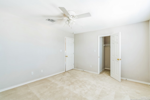 unfurnished bedroom featuring light carpet, a closet, ceiling fan, and a walk in closet