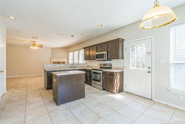 kitchen with light tile patterned flooring, hanging light fixtures, a kitchen island, appliances with stainless steel finishes, and ceiling fan