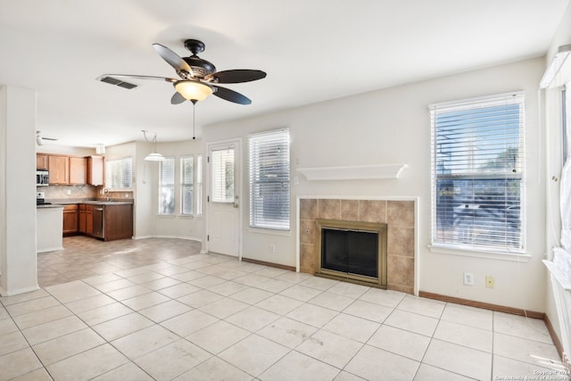 unfurnished living room featuring ceiling fan, light tile patterned flooring, sink, and a tile fireplace