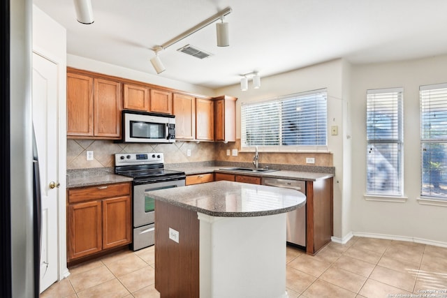 kitchen with light tile patterned floors, sink, stainless steel appliances, a center island, and decorative backsplash