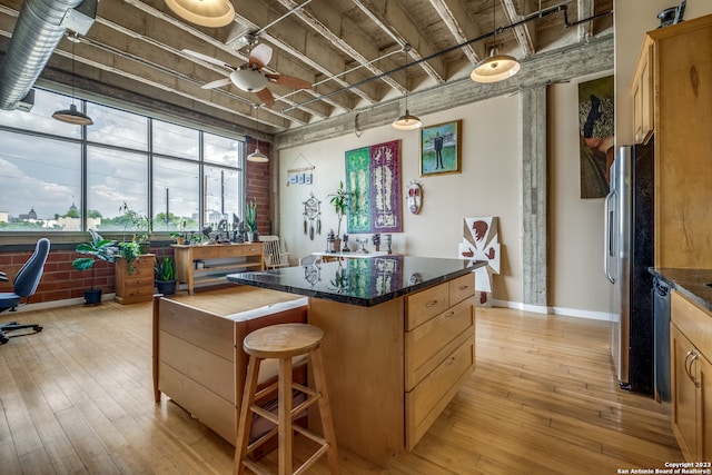 kitchen with light wood-type flooring, a kitchen island, ceiling fan, brick wall, and stainless steel fridge