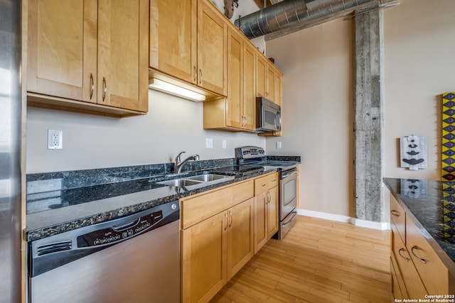 kitchen with stainless steel appliances, sink, dark stone counters, and light hardwood / wood-style flooring