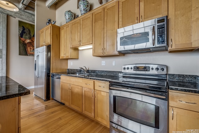 kitchen featuring dark stone countertops, appliances with stainless steel finishes, sink, and light hardwood / wood-style flooring