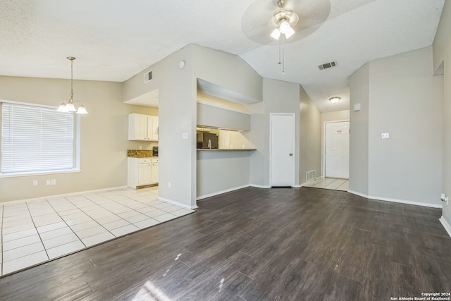 unfurnished living room with light hardwood / wood-style flooring, lofted ceiling, a textured ceiling, and ceiling fan with notable chandelier