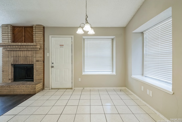 unfurnished dining area with a textured ceiling, light tile patterned floors, a chandelier, and a brick fireplace