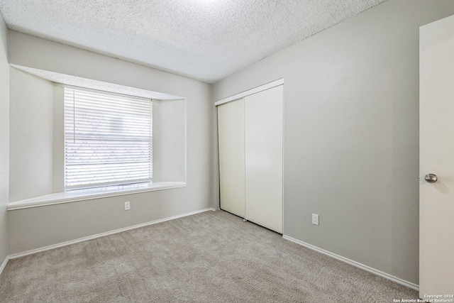 unfurnished bedroom with a textured ceiling, light carpet, and a closet