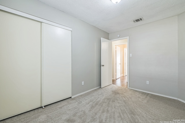 unfurnished bedroom featuring a textured ceiling, light carpet, and a closet