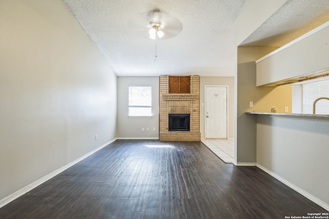 unfurnished living room with a textured ceiling, dark hardwood / wood-style floors, sink, a brick fireplace, and ceiling fan