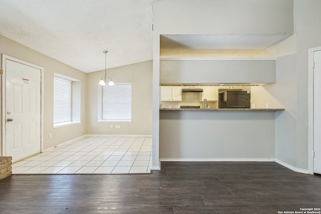 kitchen featuring black fridge, lofted ceiling, a textured ceiling, decorative light fixtures, and dark wood-type flooring