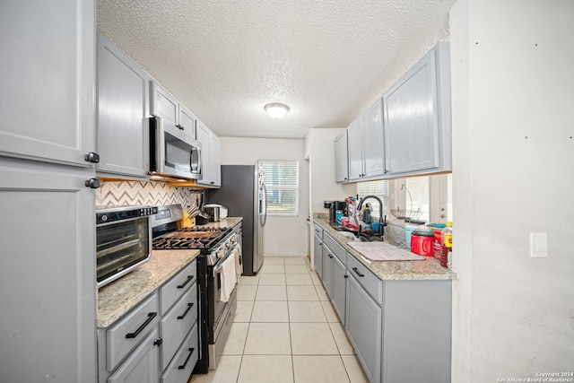 kitchen featuring light tile patterned flooring, sink, a textured ceiling, backsplash, and stainless steel appliances