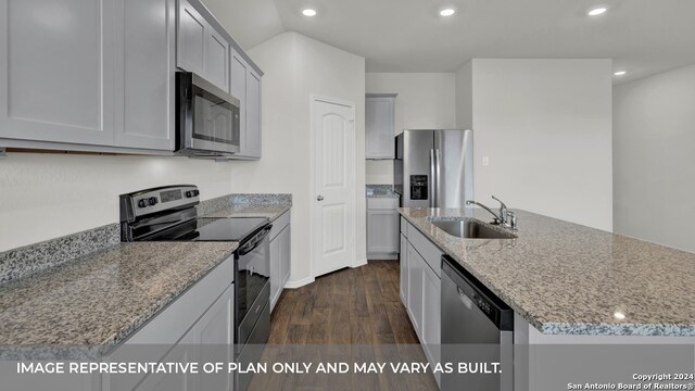 kitchen with light stone countertops, a center island with sink, appliances with stainless steel finishes, and dark hardwood / wood-style floors