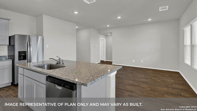 kitchen featuring dark wood-type flooring, sink, stainless steel appliances, a center island with sink, and light stone countertops