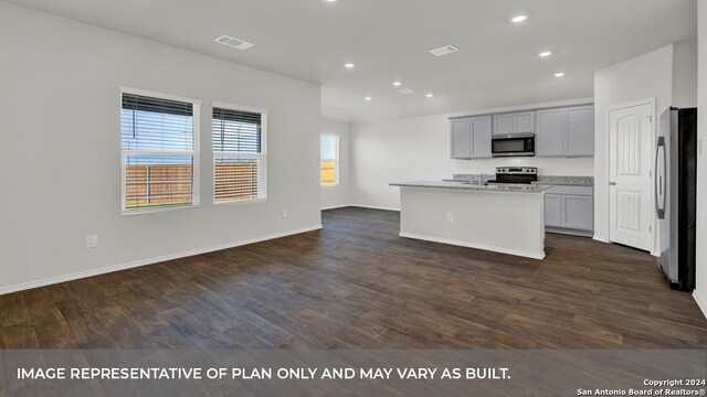 kitchen featuring an island with sink, gray cabinetry, appliances with stainless steel finishes, dark hardwood / wood-style floors, and light stone countertops