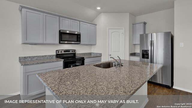 kitchen featuring appliances with stainless steel finishes, light stone counters, dark hardwood / wood-style flooring, a center island with sink, and sink