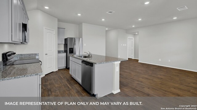 kitchen with dark wood-type flooring, light stone countertops, stainless steel appliances, a center island with sink, and sink