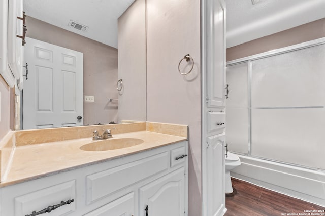 full bathroom featuring toilet, hardwood / wood-style flooring, vanity, and combined bath / shower with glass door