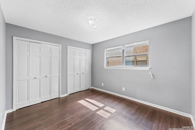 unfurnished bedroom with multiple closets, a textured ceiling, and dark hardwood / wood-style flooring