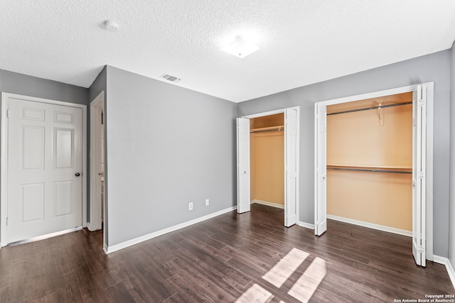 unfurnished bedroom with two closets, a textured ceiling, and dark wood-type flooring